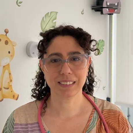 Retrato de la Dra. Alejandra Paola Levy, de pelo rizado y anteojos, con estetoscopio, en el consultorio.