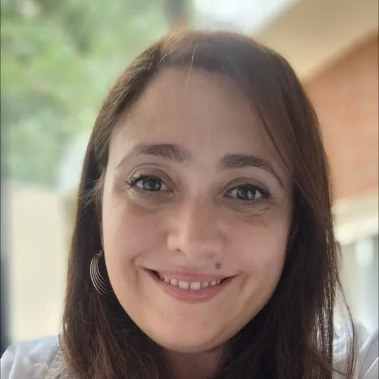 Retrato de la Dra. María Victoria Tarruella, de pelo largo oscuro y guardapolvo claro, sonriendo al aire libre.